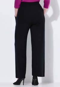 Zwarte wijde broek met een gladde textuur, voorzien van zijzakken en een hoge taille. Gecombineerd met zwarte peep-toe hakken.
