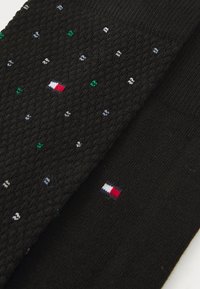 Chaussettes noires avec un motif texturé et des points multicolores. Un petit logo avec des rayures rouges, blanches et bleues est visible.