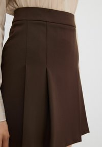 Gonna a pieghe marrone realizzata in tessuto liscio, con vita ben aderente e design fluido a forma di A.