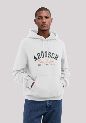Weißer Hoodie aus weichem Stoff mit großer Fronttasche, versehen mit einem schwarzen und orangefarbenen Textdesign. Kombiniert mit blauen Jeans.