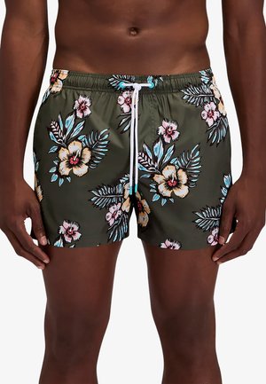 Torso y parte superior de las piernas masculinas con pantalones cortos de baño verde oliva con estampado tropical floral colorido y cordón blanco atado a la cintura.