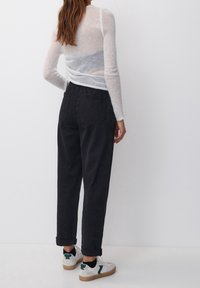 Maglione lungo e leggero con maniche lunghe di colore bianco con accenti grigi, abbinato a pantaloni neri a vita alta e sneakers bianche con dettagli verdi.