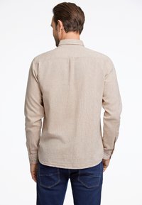 Camisa de manga larga beige claro con tejido texturizado, puños abotonados y dobladillo recto, combinada con vaqueros azul oscuro.