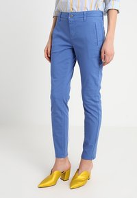 Světle modré, úzké kalhoty z bavlny, s jednou přední kapsou a zipem v pase. Spárováno se žlutými vyššími mules.