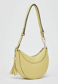 Sac à main jaune en simili cuir en forme de croissant avec des accents noirs, une bandoulière et un détail à pompon, doté d'une fermeture éclair.