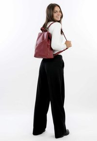 Roter Leder-Rucksack mit strukturiertem Design, verstellbaren Trägern und strukturiertem Finish, getragen von einem Model in schwarzen weiten Hosen.