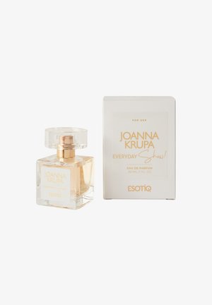 Przezroczysta szklana butelka perfum z okrągłym korkiem, jasnokremowy płyn, oznaczona napisem "Joanna Krupa Everyday Show!" oraz złotymi akcentami, w białym pudełku.