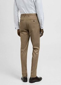 Pantaloni bej deschiși, croiți, cu un model texturat, ajustați, și buzunare pe spate. Asortați cu o cămașă albă și pantofi închisi la culoare.