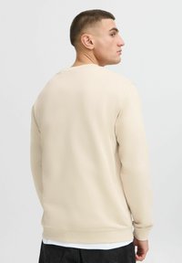 Felpa beige chiaro realizzata in tessuto morbido, con collo rotondo, maniche lunghe e polsini a costine. Texture liscia senza motivi visibili.