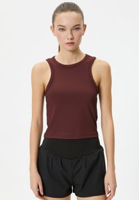 Burgundy ärmlös träningslinne med rundad halsringning, tillverkat av lättviktsmaterial. Kombinerad med svarta shorts med hög midja.