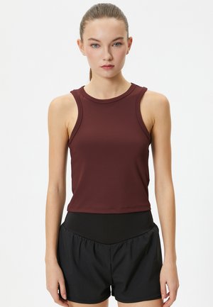 Top atlético sin mangas burdeos con un escote redondeado, hecho de una tela ligera. Combinado con pantalones cortos negros con una cintura alta.