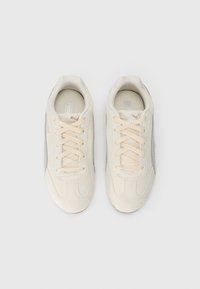 Sneakers in suede beige con una superficie liscia, dotati di lacci beige chiaro, un design semplice e un pannello accentato grigio su un lato.
