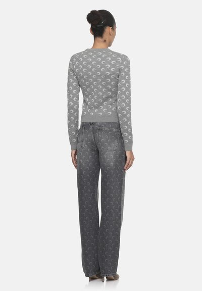 Maglione grigio con motivo a luna crescente; abbinato a jeans grigi a gamba larga che mostrano un motivo simile.