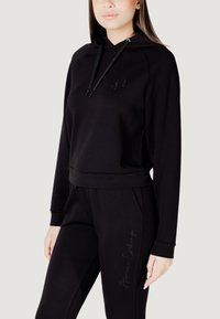 Czarna bluza z kapturem ze sznurkiem, z dyskretnym logo na klatce piersiowej, w zestawie z czarnymi spodniami dresowymi z kursywnym napisem. Miękki materiał, luźny krój.