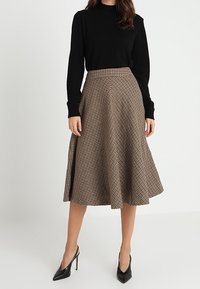 Ruskea ja musta ruutukuvioinen midihame, jossa liehuva malli; yhdistetty mustaan neuleeseen ja korkeakorkoisiin kenkiin, ja siinä on sileä pinta.