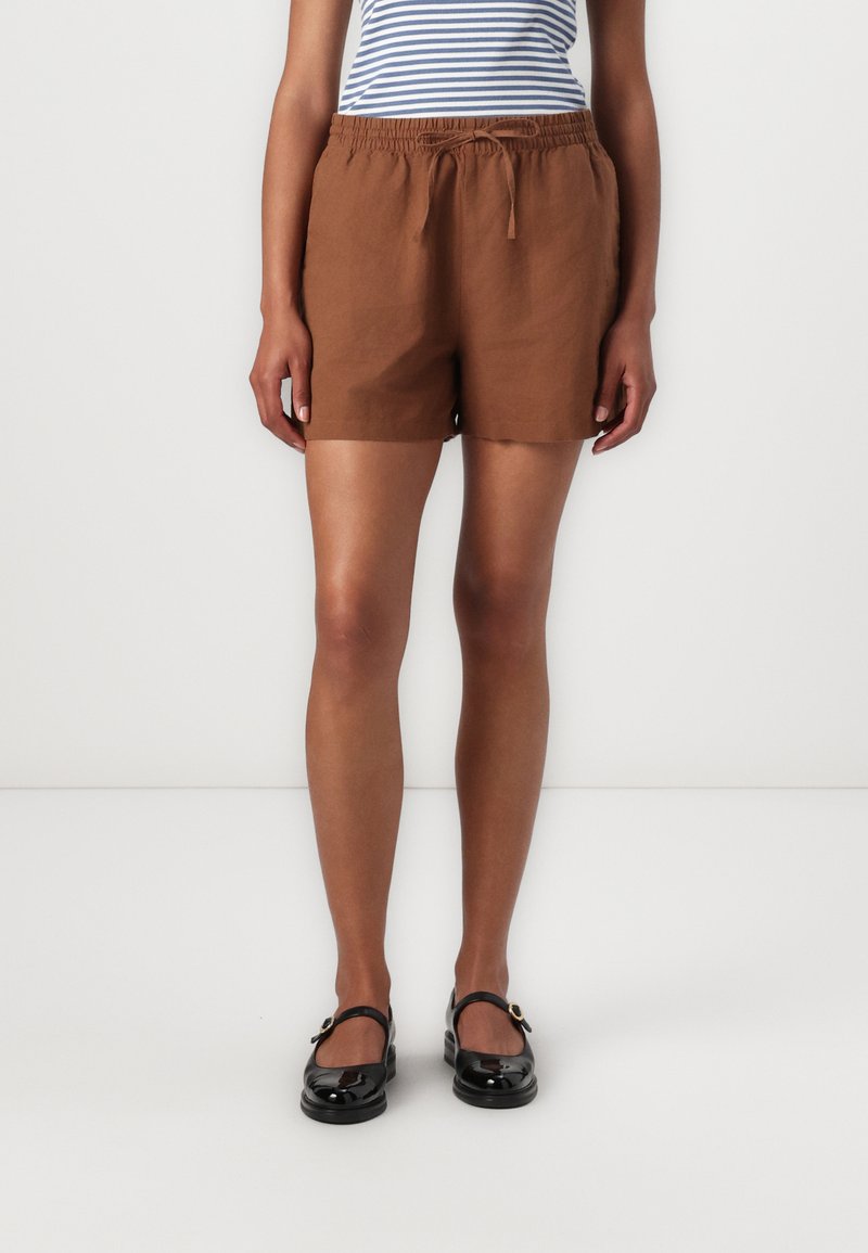 Brune linshorts med elastisk liv og snor, med en avslappet passform og hemmede kanter, kombinert med svarte lakklerret sko.