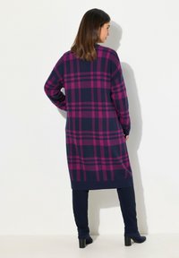 Lång marinblå klänning med ett djärvt magenta rutig mönster, med långa ärmar och rak skärning, parat med mörka leggings och klackboots.