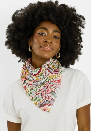 Mujer con cabello rizado y voluminoso que lleva pendientes de aro dorados, una camisa blanca y un pañuelo colorido con estampado alrededor del cuello.