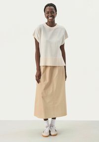 Lys beige stribet top med korte ærmer og en bred kant, parret med en lang beige nederdel. Båret med hvide sokker og sneakers.