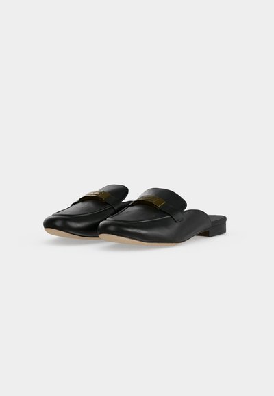 Ζευγάρι μαύρα δερμάτινα παπούτσια τύπου slip-on με χαμηλά τακούνια και χρυσές μεταλλικές λεπτομέρειες σε λευκό φόντο.