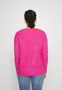 Fuchsia gerippter Strickpullover mit langen Ärmeln, rundem Ausschnitt und seitlichen Schlitzen, kombiniert mit hellblauen Jeans.