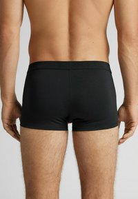 Czarne bokserki wykonane z gładkiej tkaniny, wyposażone w miękki pas i dopasowany krój. Faktura wydaje się lekko matowa.