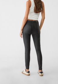 Černé skinny džíny s vysokým pasem, vyrobené z elastického materiálu, mají dvě zadní kapsy a hladkou texturu, doplněné béžovými teniskami.