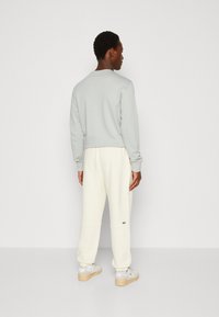 Lys grå sweatshirt med rund hals, parret med cremefarvede sweatpants. Har et diskret grønt logo på bukserne og hvide sneakers.