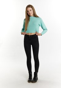 Mentazöld, ribbelt texture-rel rendelkező, rövidített pulóver, fekete skinny farmerral és fekete, fűzős bokacsizmával párosítva, fehér háttér előtt.