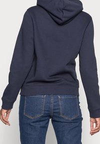 Felpa con cappuccio blu navy con tasca a marsupio, maniche e orlo a costine, vista da dietro, abbinata a jeans in denim blu.