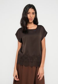 Καφέ σατέν μπλούζα με κοντά μανίκια, με δαντελένιο τελείωμα στο κάτω μέρος. Λεία υφή με στρογγυλή λαιμόκοψη και άνετη γραμμή.