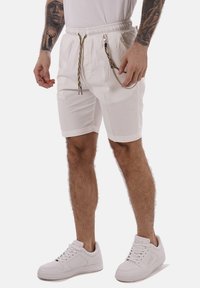 Pantalones cortos blancos de algodón con cintura elástica y cordón, que presentan cadenas decorativas. Combinados con zapatillas blancas.