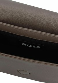 Bolso de cuero marrón texturizado con una solapa abierta que revela un interior negro y una etiqueta interna que dice "BOSS".