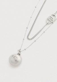 Srebrna naszyjnik z okrągłym wisiorkiem z wypukłym logo. Projekt zawiera dwa style łańcuszka: jeden płaski i jeden koralikowy.