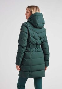 Chaqueta tipo puff verde con capucha, cintura ajustada y diseño acolchado. Presenta un parche de logo en el hombro y una textura lisa y brillante.