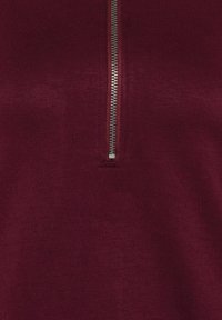 Nahaufnahme eines kastanienbraunen Stoffes mit einem silbernen Metallreißverschluss, der teilweise geöffnet ist.
