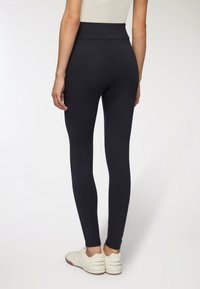 Czarne legginsy o wysokim stanie, wykonane z elastycznej tkaniny, dopasowany krój, gładka faktura, w połączeniu z białymi butami sportowymi.