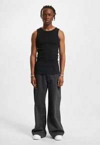 Top negro acanalado combinado con jeans de pierna ancha en gris oscuro y zapatillas blancas. El modelo se encuentra de frente con los brazos relajados a los lados.