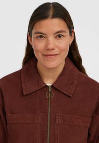 Brown corduroy jacket with a zip front, flat collar, two front pockets, and gold-toned hardware, featuring a ribbed texture.