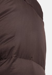 Doudoune marron avec une texture lisse et brillante. Présente une couture horizontale le long de la section inférieure et un col haut.