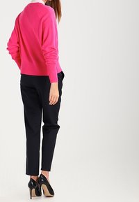 Fuchsia gestrickter Pullover mit langen Ärmeln, kombiniert mit schwarzen schmal geschnittenen Hosen und schwarzen High Heels. Glatte Textur, lässige Passform.