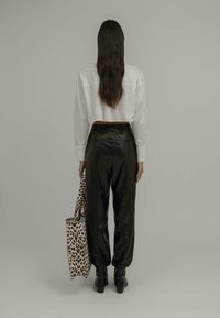 Skraćena bijela košulja, crne kožne hlače i masivne crne čizme. Nosite torbu s leopard uzorkom. Jednostavna siva pozadina.