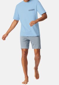 Hellblaues Baumwoll-T-Shirt mit kurzen Ärmeln und einer Tasche; kombiniert mit gemusterten Shorts in Marineblau und Weiß. Schuhe sind nicht sichtbar.