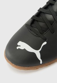 Sort sportsko med tekstureret syntetisk overdel, der har et hvidt Puma-logo og sorte snørebånd. Sålen er brun og giver godt greb.