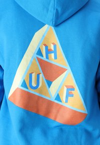 Blue hoodie featuring a triangular graphic in pastel colors with the letters "H," "U," and "F." Soft texture, casual design, and spacious hood.
