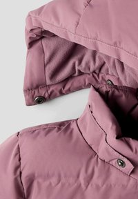 Pehmeast roosa värvi soe jope fleecest voodriga kapuutsiga. Omab kõrget kraed ja hõbedast pressnuppu sulgemiseks, esitleb sileda kangatekstuuri.