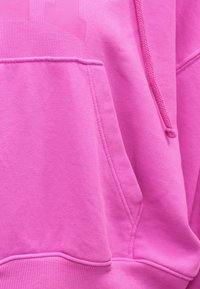 Sweat à capuche rose vif avec poche kangourou sur le devant et cordon de serrage assorti, montrant un gros plan sur la texture du tissu et les détails des coutures.