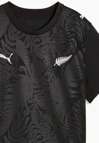 T-shirt de sport noire avec un motif tigre subtil, emblème de fougère blanche sur la poitrine, et logo Puma blanc sur l'épaule droite et la poitrine gauche.