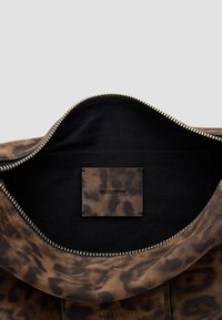 Bolso de cuero con un estampado de leopardo en tonos marrón y negro, que presenta un zipper dorado y un interior negro con una etiqueta de cuero de la marca.