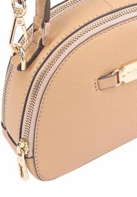 Sac à main en cuir beige avec des fermetures éclair dorées, un fermoir doré et une petite plaque de marque dorée à l'avant.